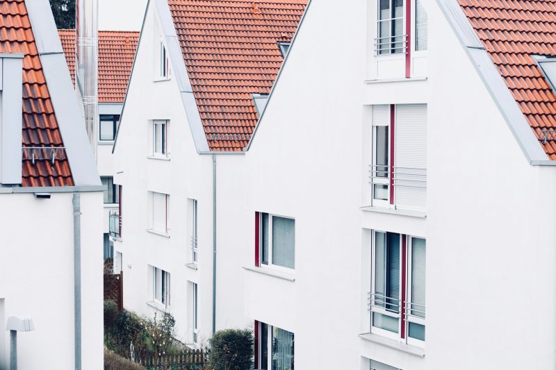 Row of modern white houses with steep, red-tiled roofs and multiple windows, closely packed together, creating a clean and orderly residential neighborhood scene.