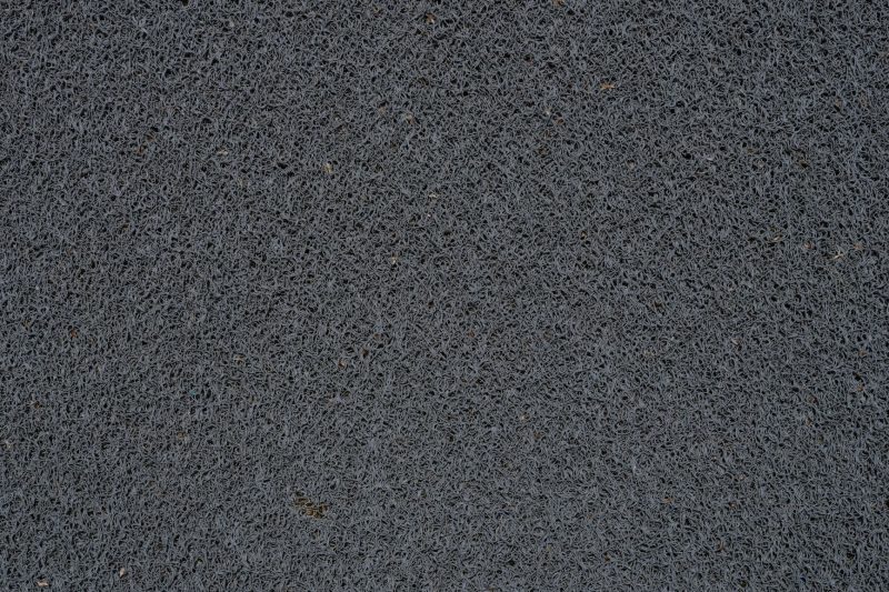 Close-up of a textured gray surface with a tangled, fibrous pattern resembling a scouring pad or rough fabric. The material appears dense and irregularly woven, giving a sense of roughness and durability.